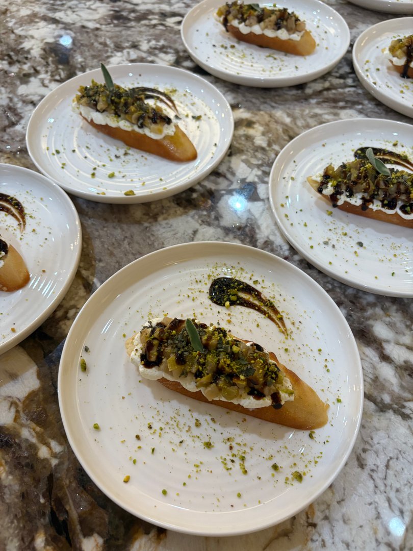 Plated roasted pear crostini with whipped ricotta and sage, drizzled with balsamic glaze.