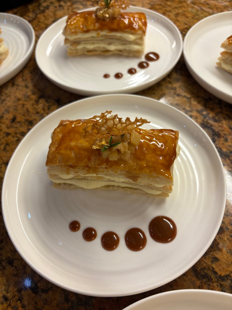 Mille-Feuille dessert with caramel glaze, garnished with gold leaf and rosemary sprig.