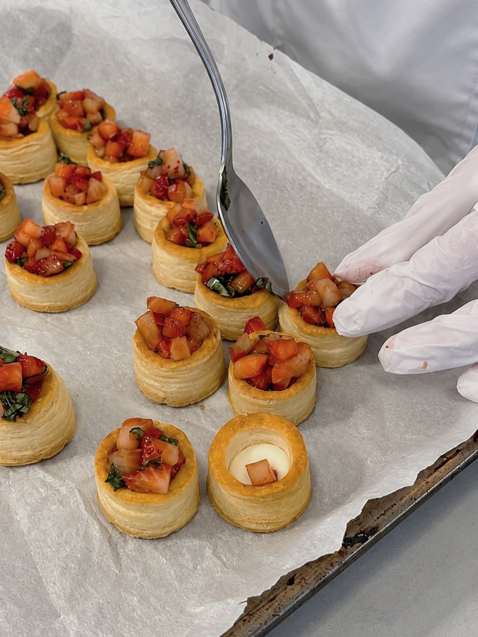 Chefs fill puff pastry vol-au-vents with cream and finish them with strawberries at the counter.