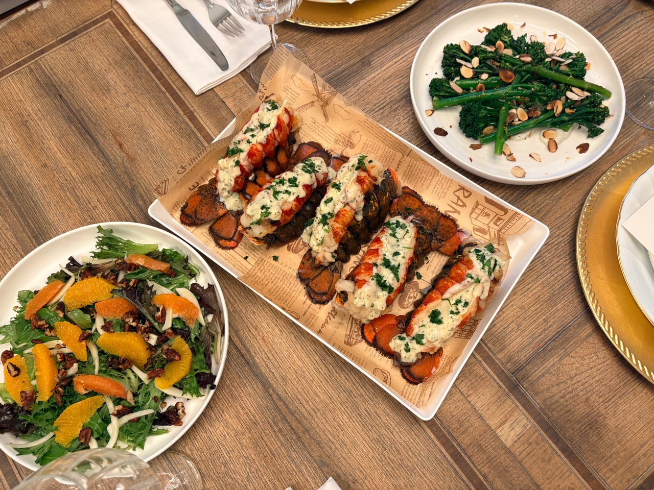 An overhead view of lobster tails, broccolini and a fennel and orange salad on the table.