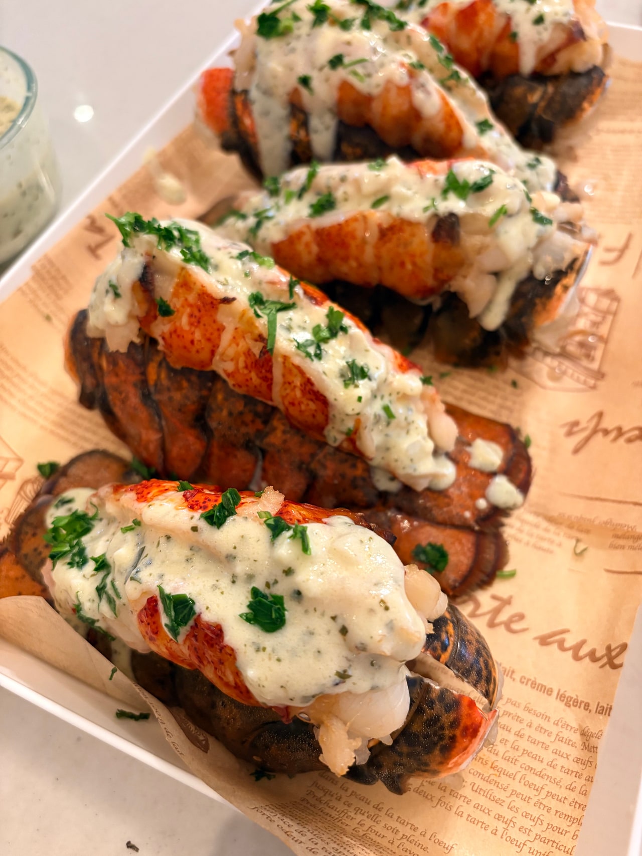 Lobster tails topped with sauce and chopped herbs on a wooden serving board.