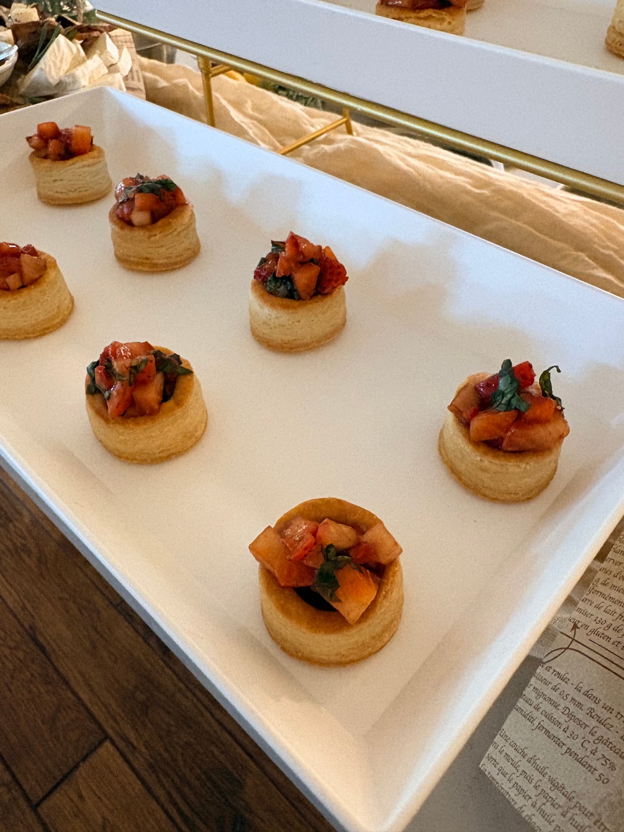 Small puff pastry vol-au-vents filled with cream and strawberries, finished with basil on a white platter.