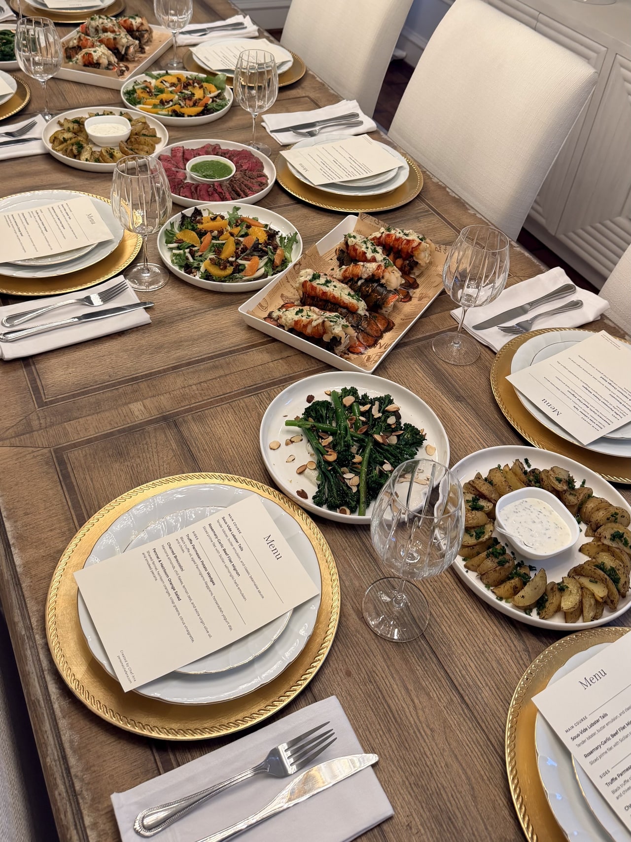 The dinner table with gold-rimmed place settings, printed menus and shared platters of lobster and vegetables.