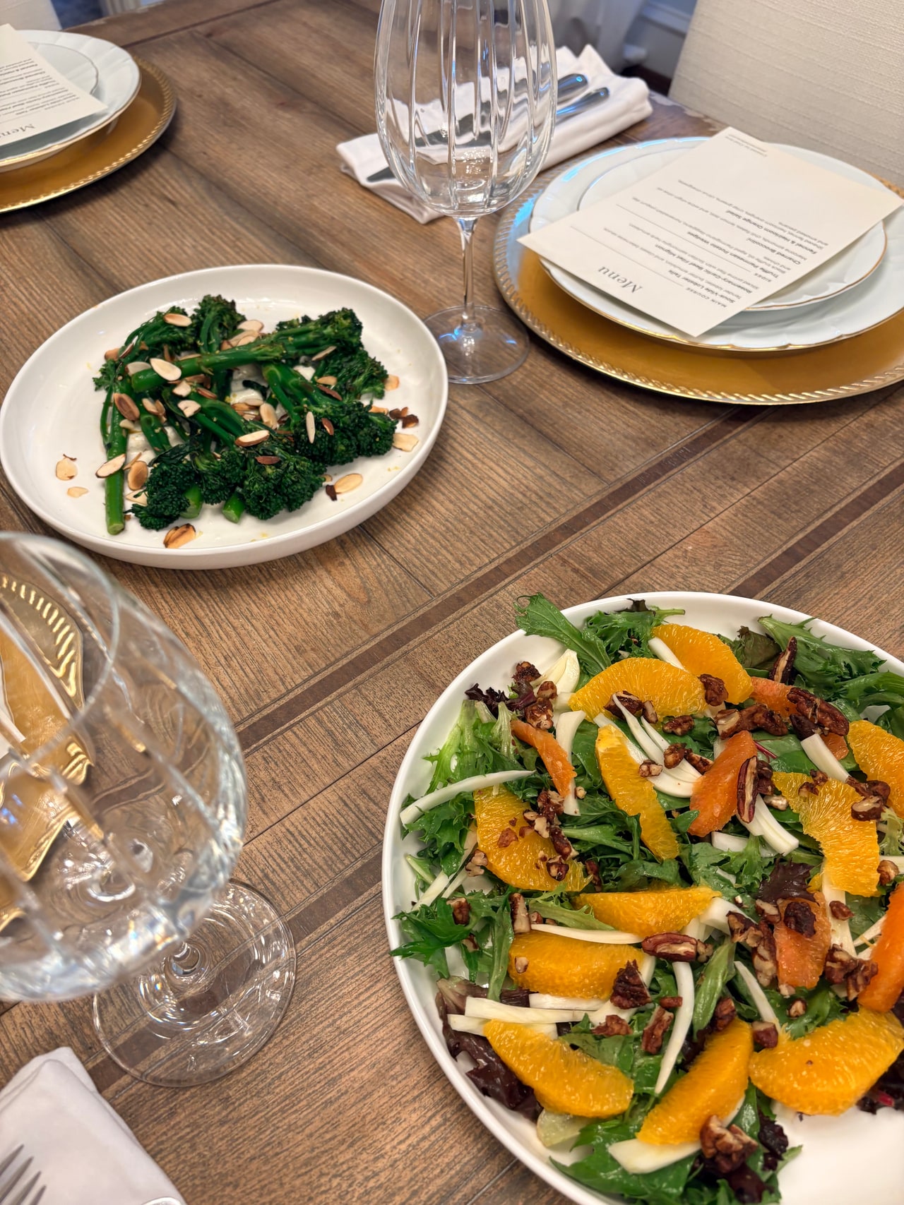 Lobster tails, broccolini and a fennel and orange salad arranged beside gold-rimmed plates on the dinner table.
