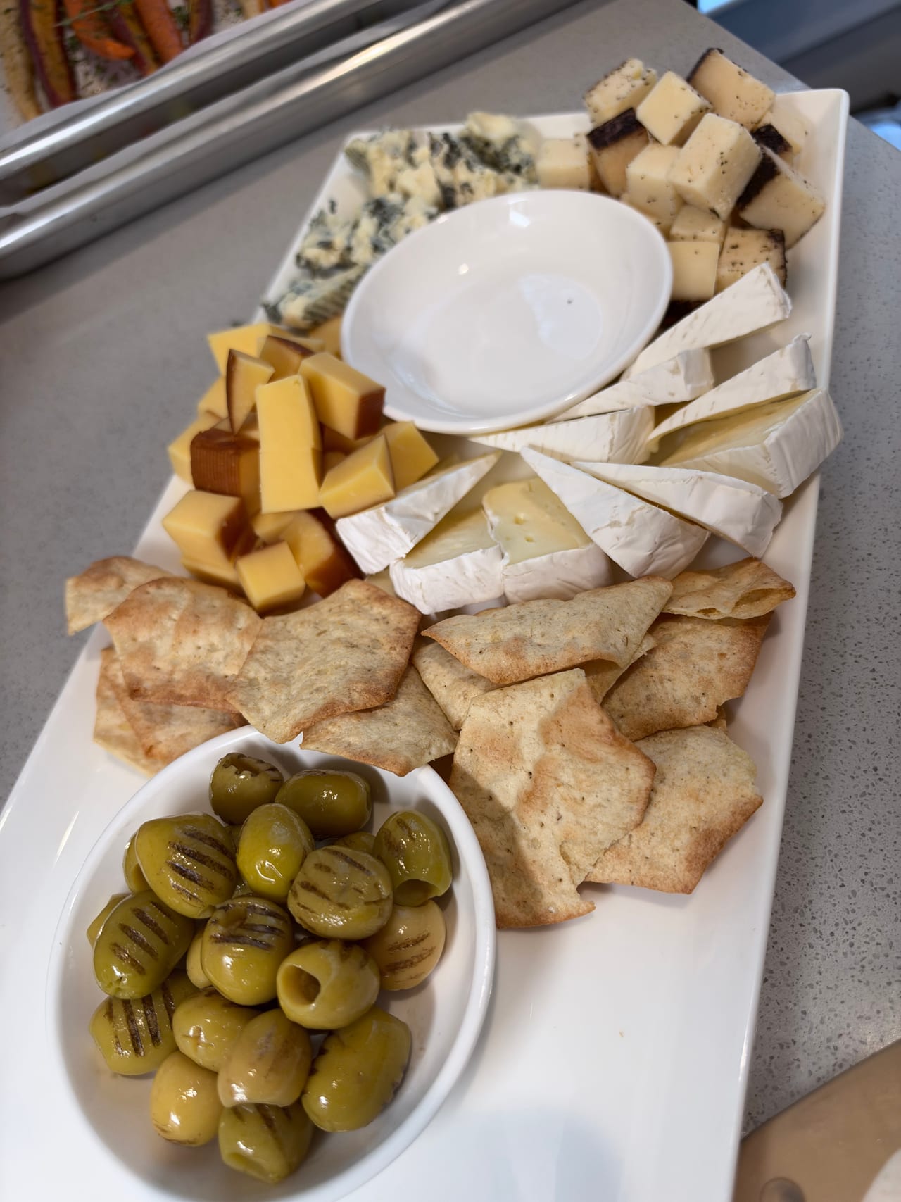 Cheese, crackers and olives arranged around a small white bowl.