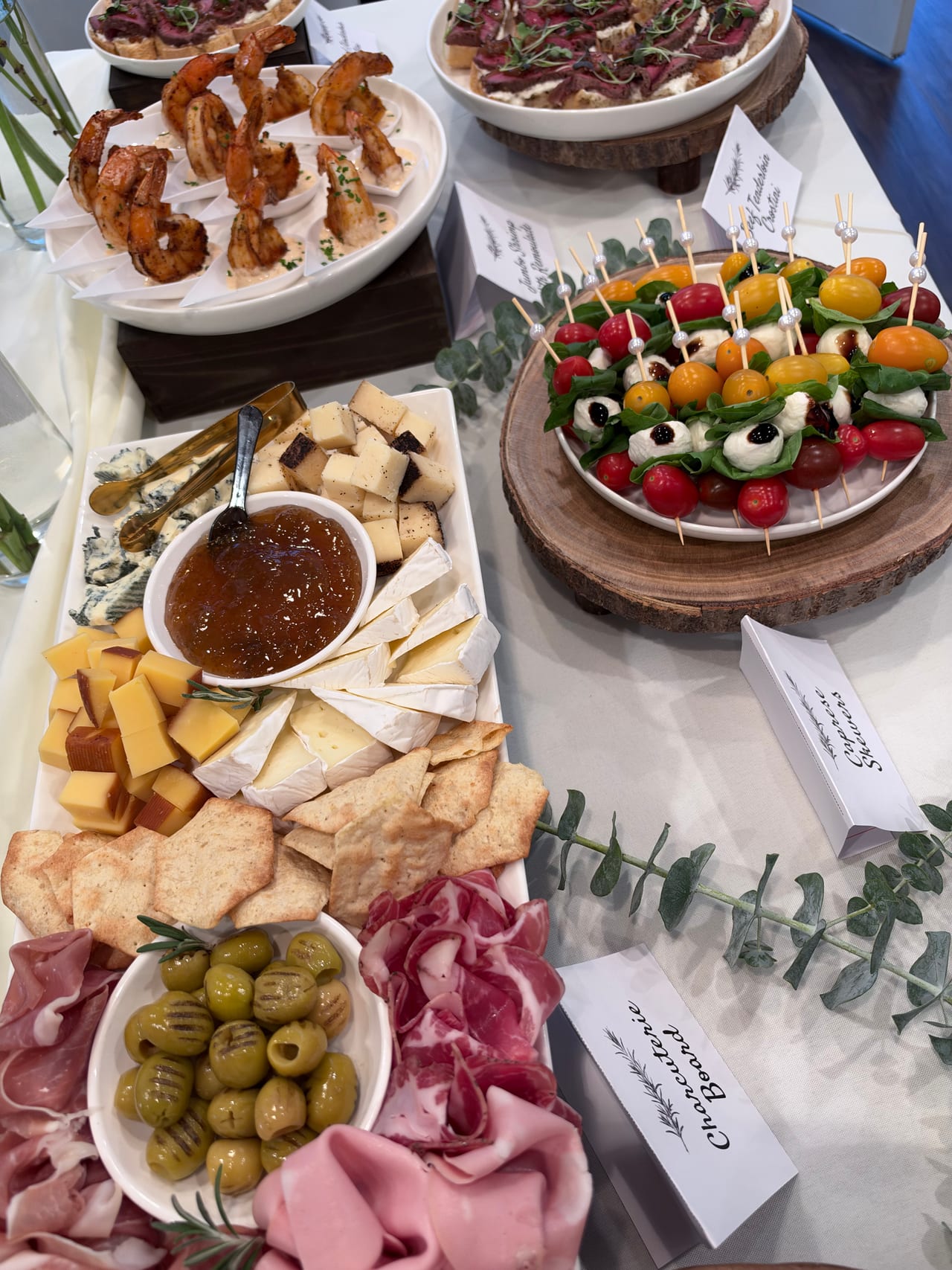 Shrimp, crostini, Caprese skewers, cheese and charcuterie on an appetizer table.