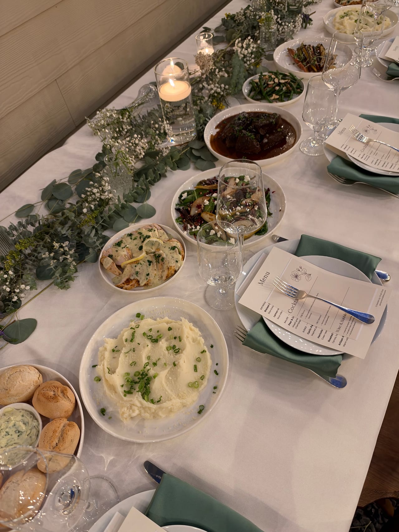 A candlelit dinner table set with shared dishes and folded green napkins.