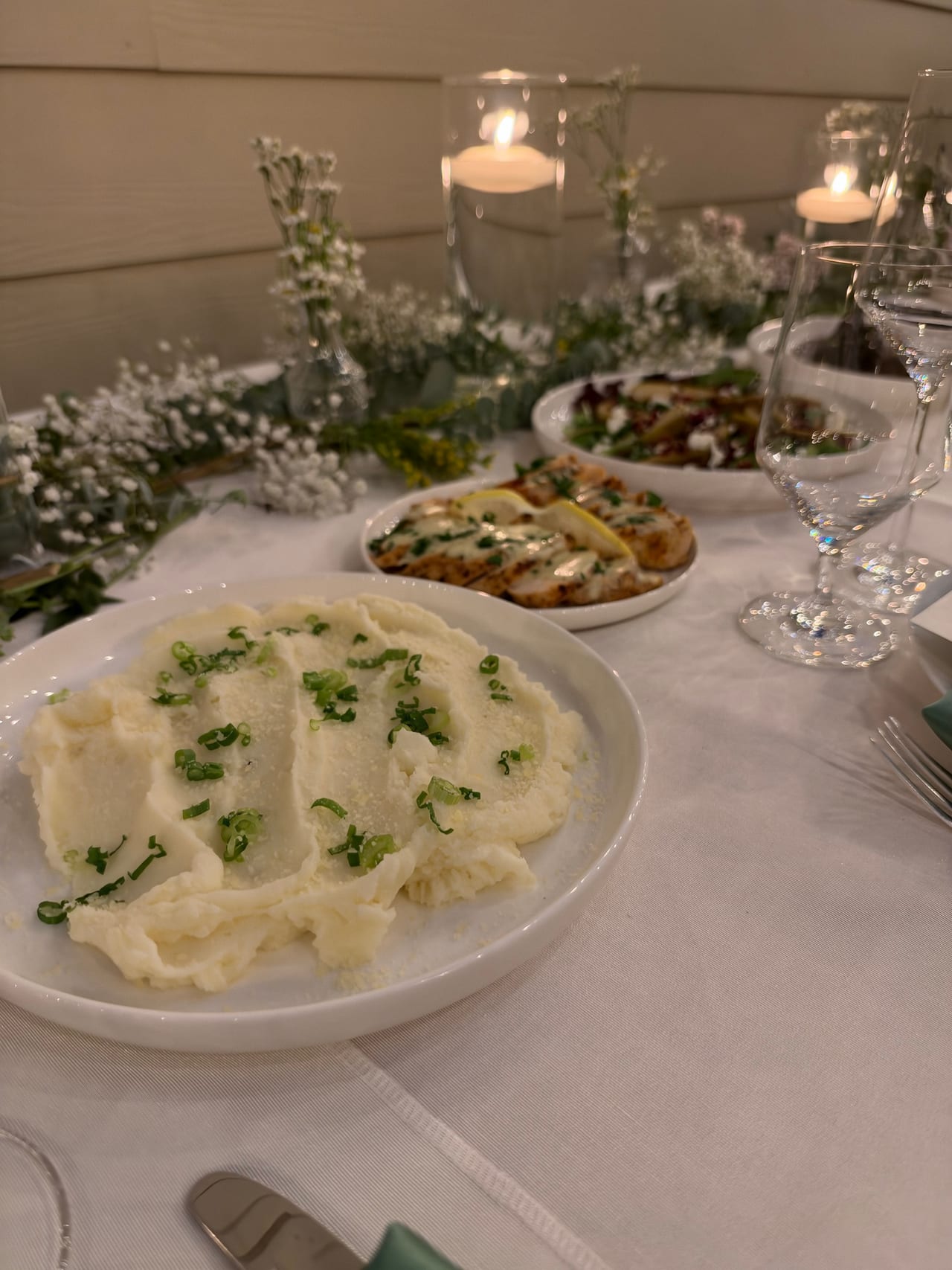 Pear salad and mashed potatoes on a long table with candles and place settings.