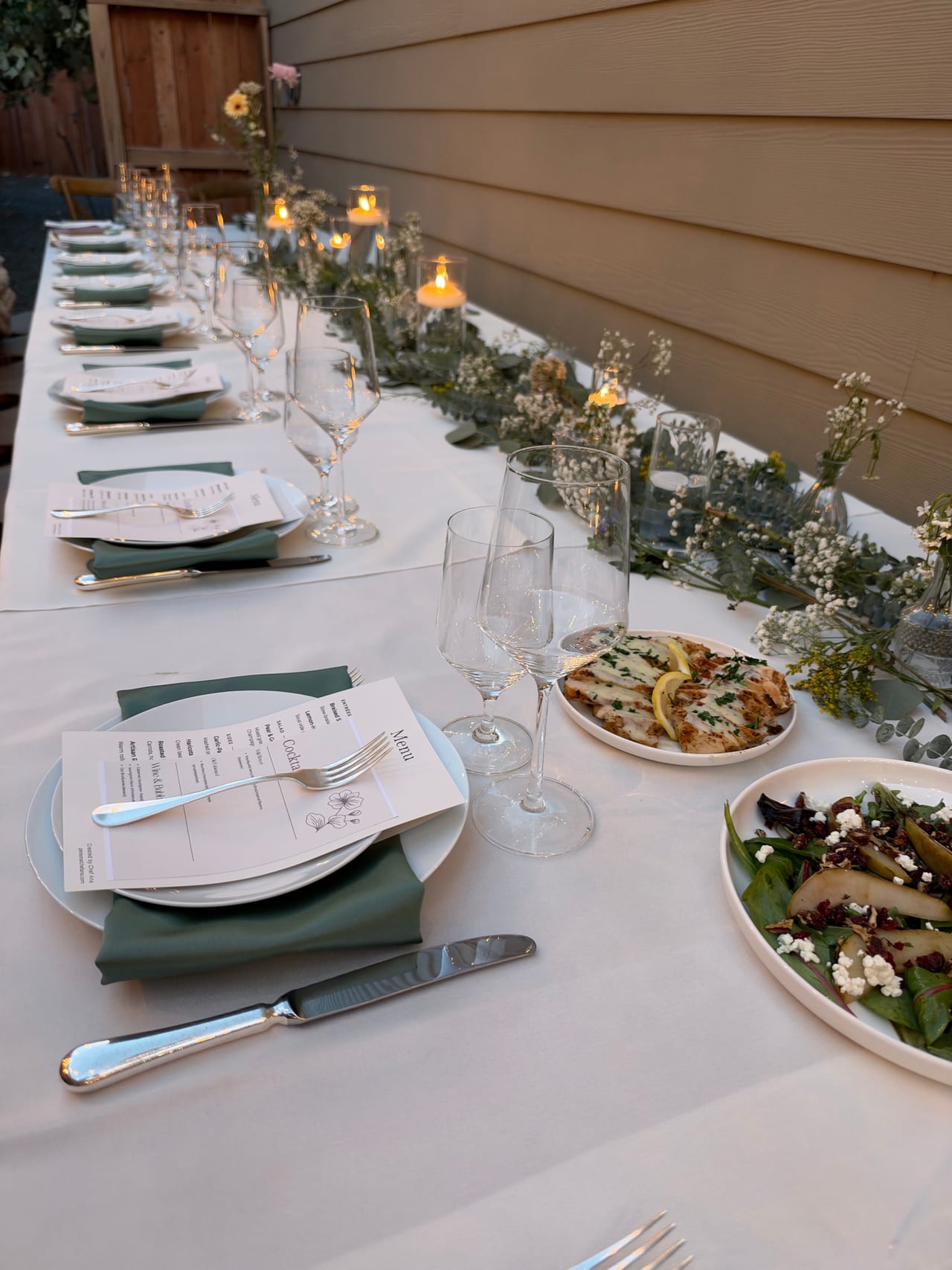 A long dinner table set with candles, green napkins and shared dishes.