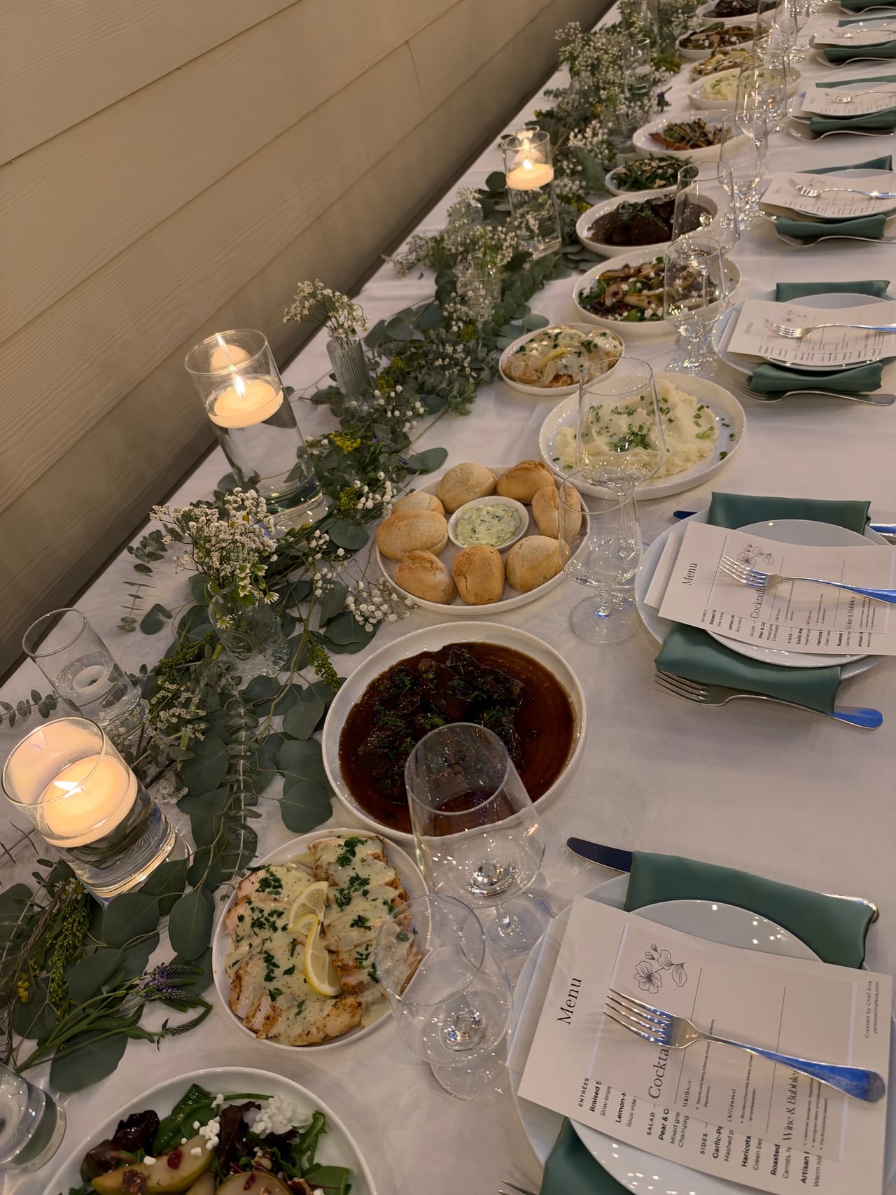 A long dinner table with candles, shared platters and place settings.