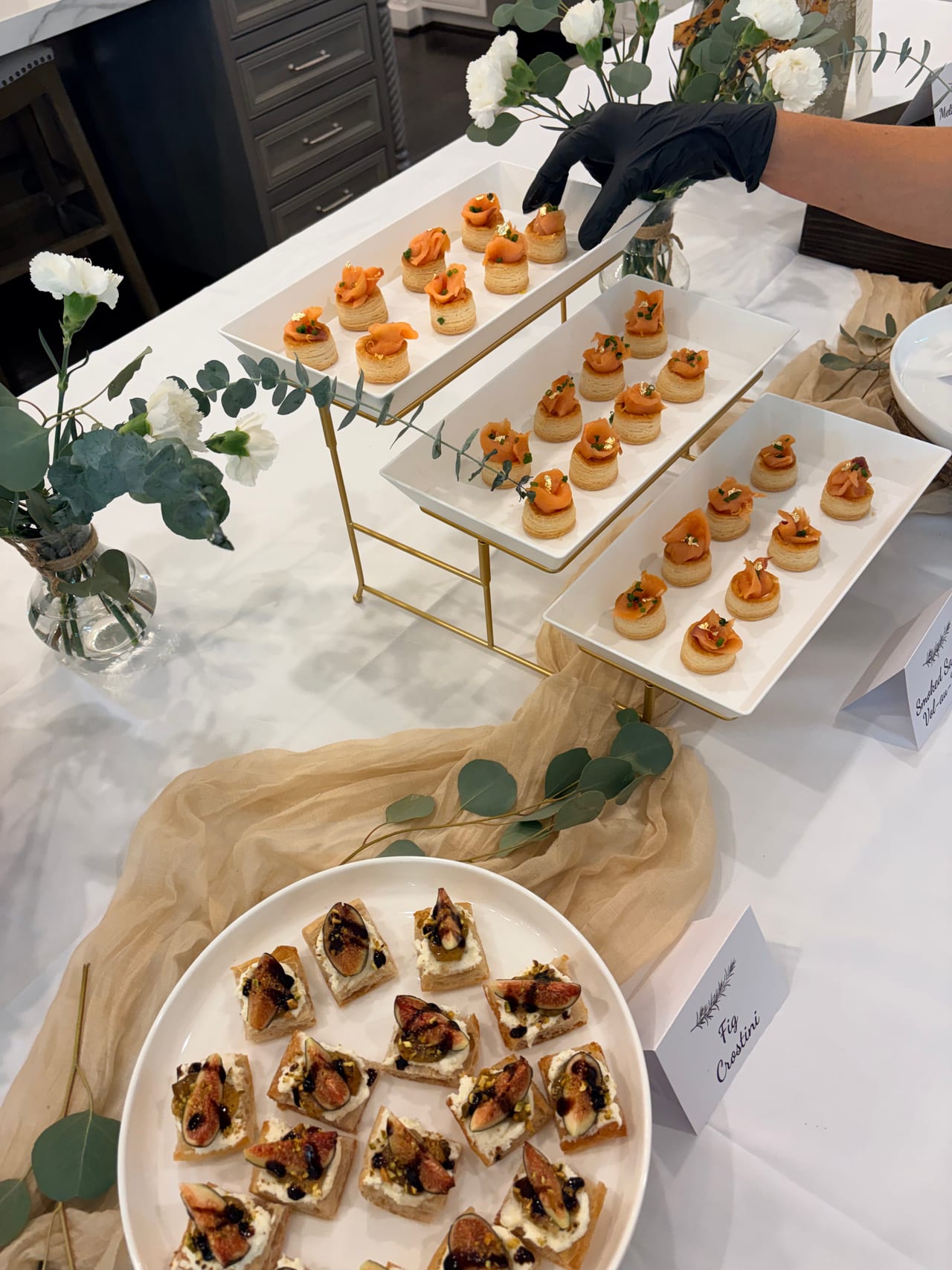 Gloved hands arrange small appetizers on a tiered display.