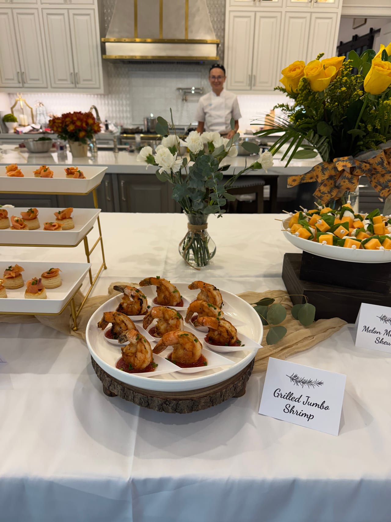 A chef stands behind the kitchen island with prepared dishes.