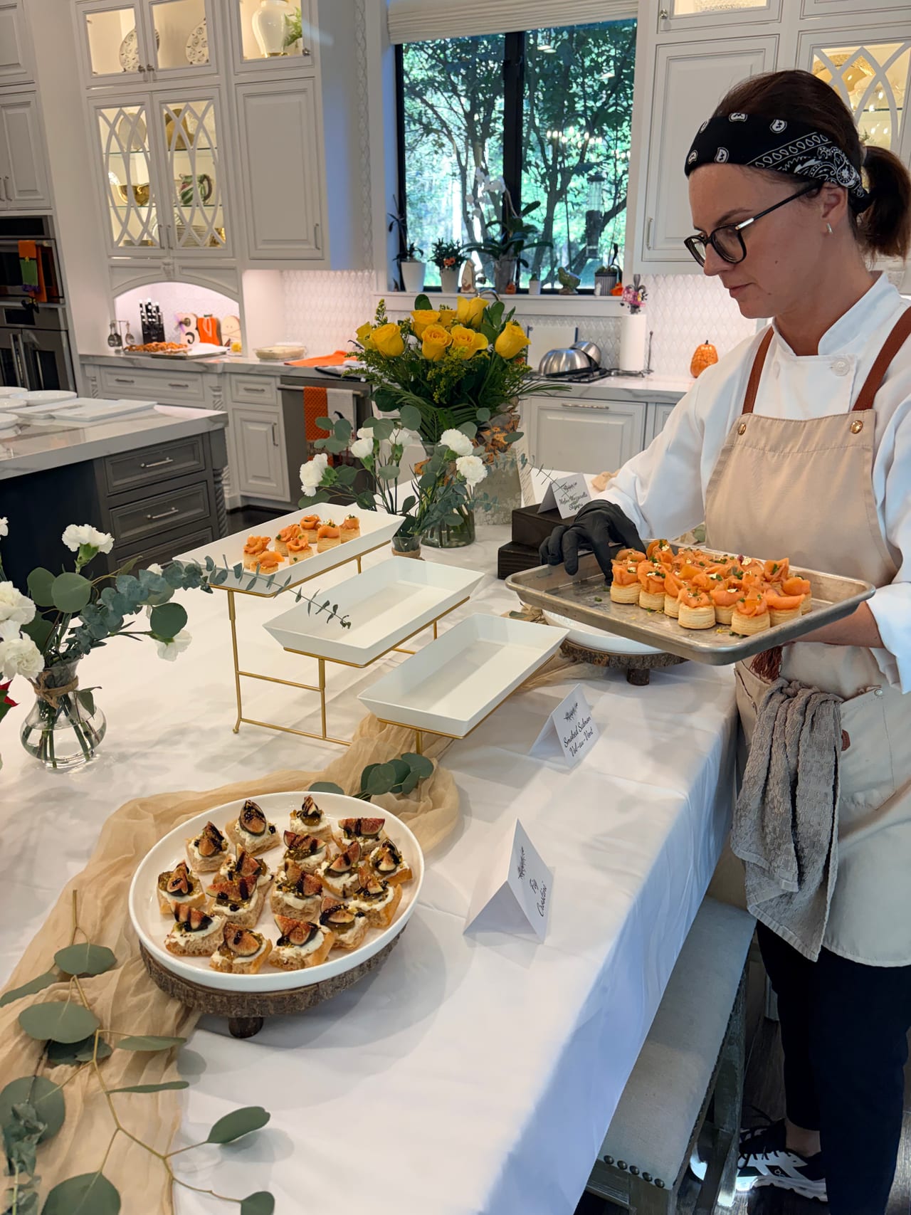 A chef carries a tray of small appetizers at a kitchen counter.