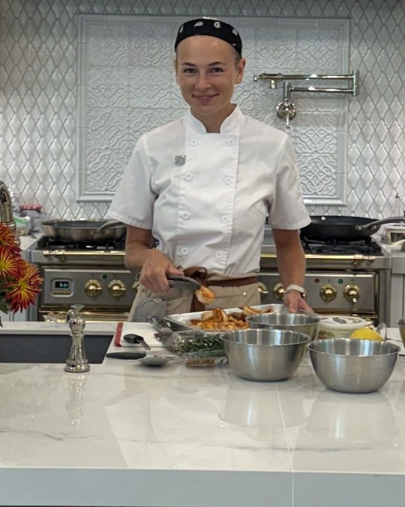 A chef stands behind a kitchen island with appetizers and flowers.
