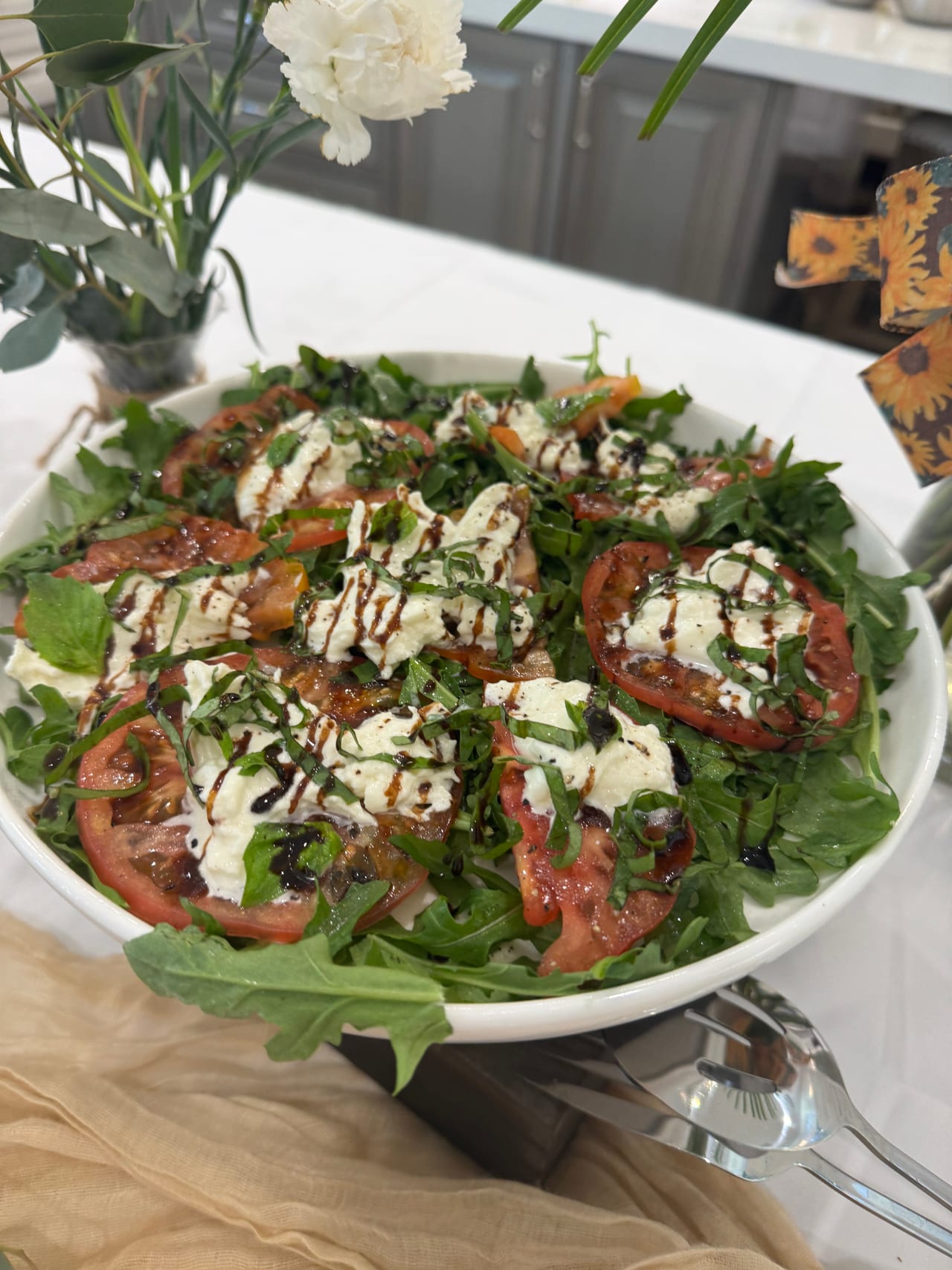 Tomato and burrata salad with greens and herbs in a white bowl.