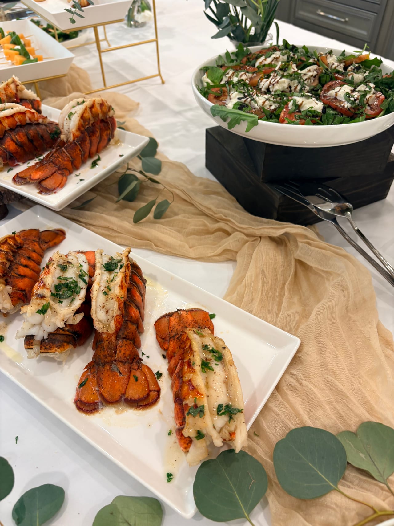 Lobster tails on a serving board beside an heirloom tomato salad.