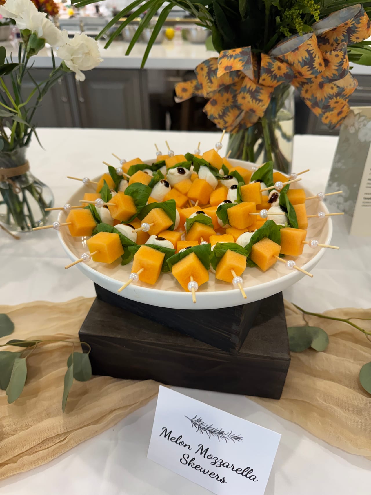 Melon and mozzarella skewers with basil on a raised platter.