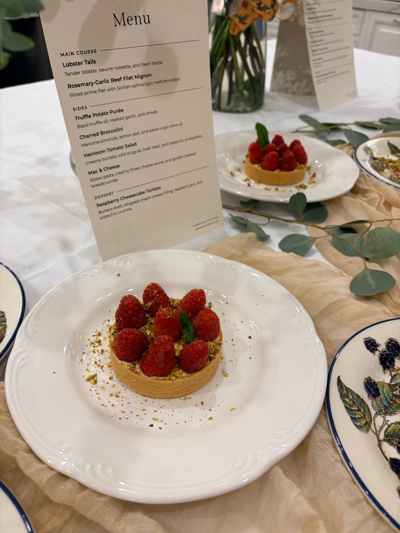 A printed dinner menu beside a raspberry tartlet on a plate.