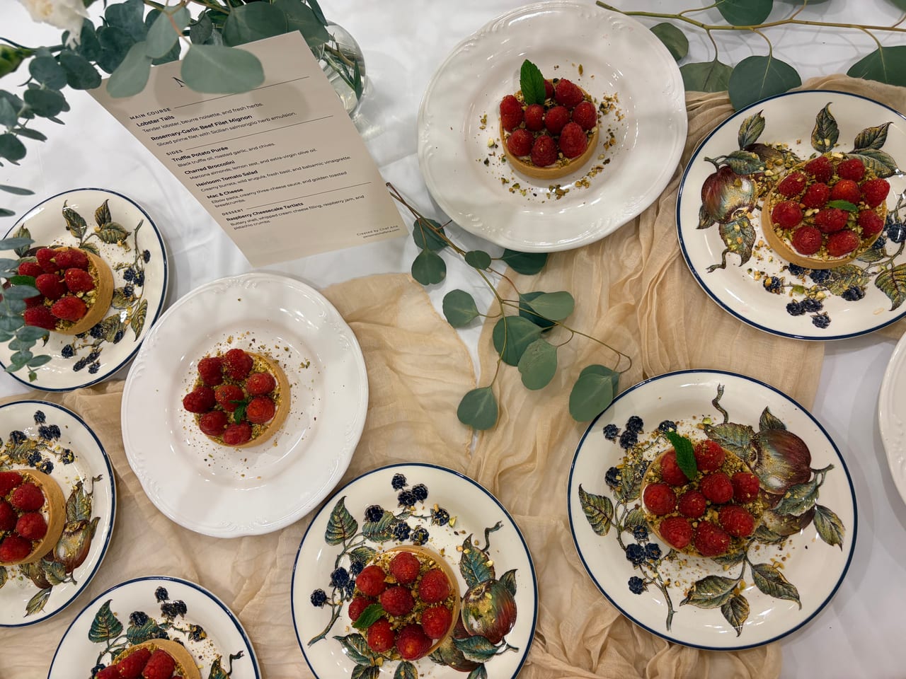 Overhead view of raspberry tartlets around a printed menu.