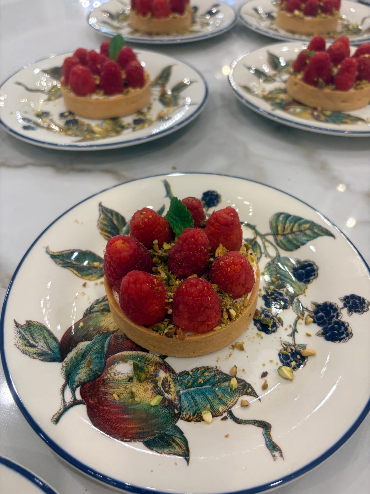A raspberry tartlet topped with berries on a decorated plate.