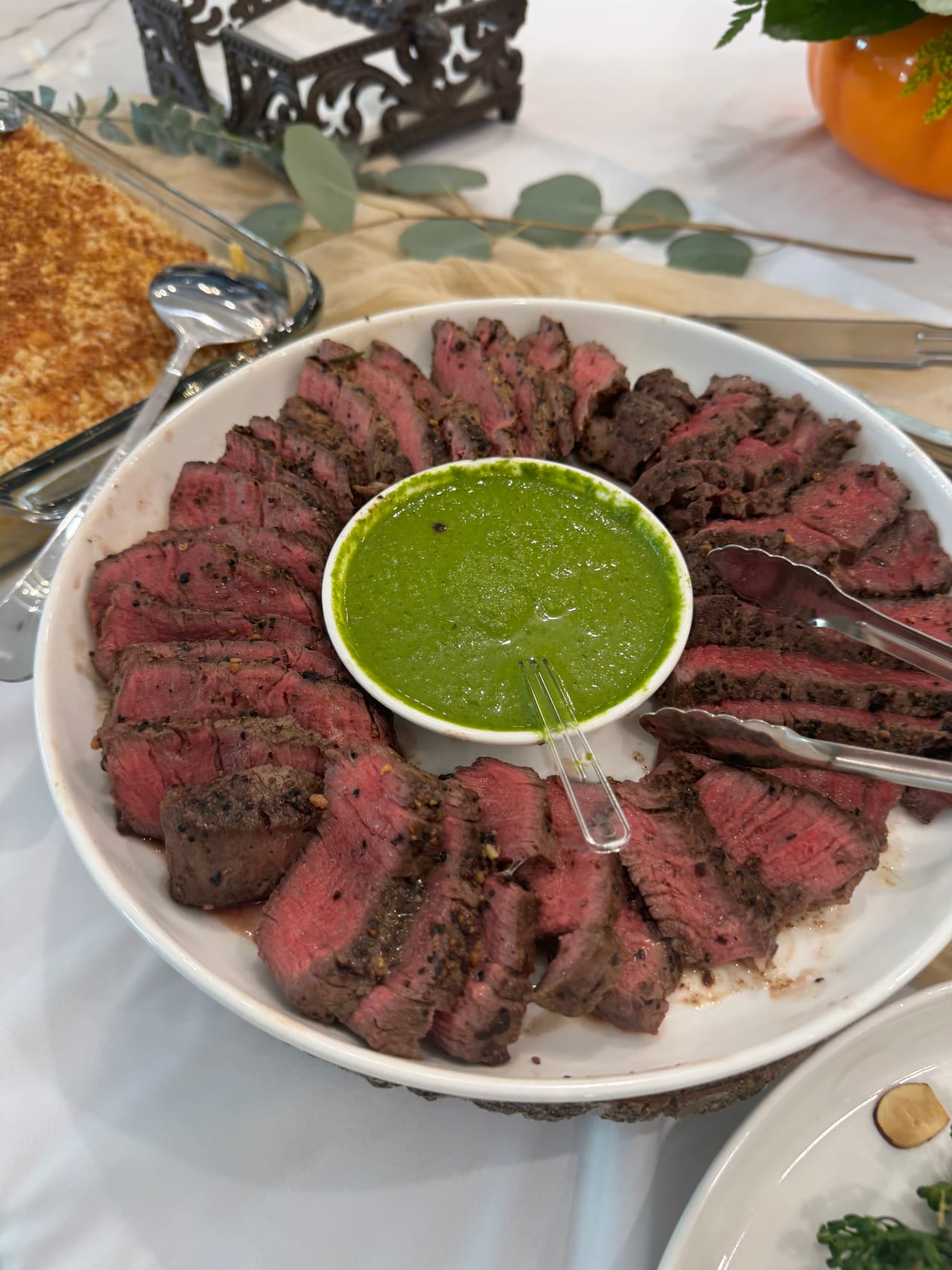 Sliced beef filet mignon arranged around a bowl of green sauce.