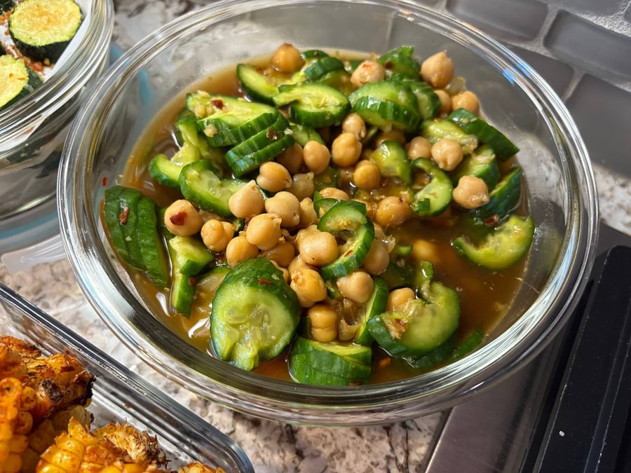 A glass bowl filled with spicy marinated sliced cucumbers and tender chickpeas in a zesty, seasoned vinaigrette dressing.