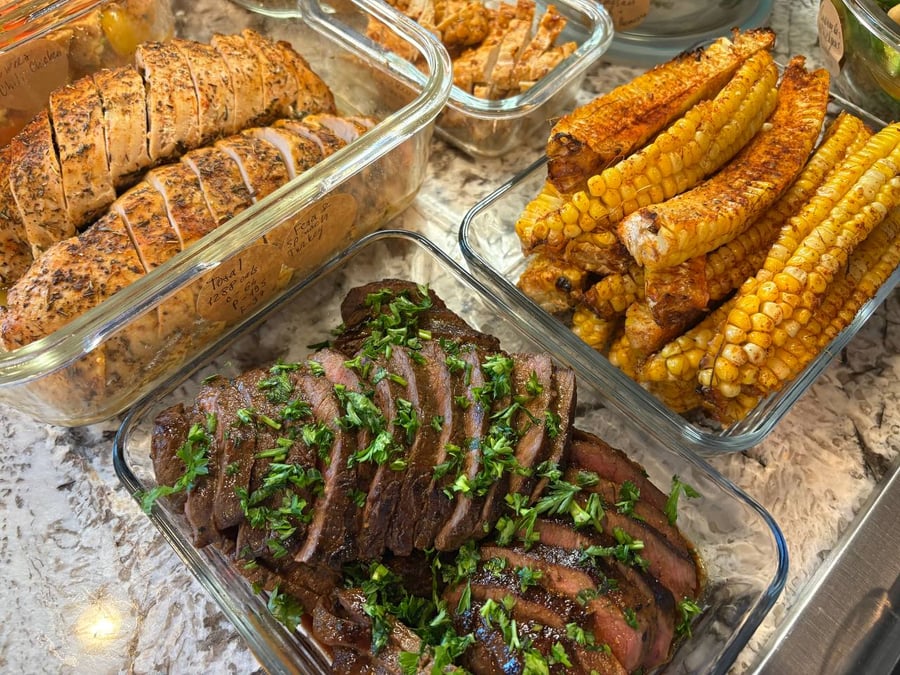 Glass containers featuring sliced herb-crusted stuffed turkey, vibrant paprika corn ribs, and ginger soy steak garnished with fresh chopped herbs.