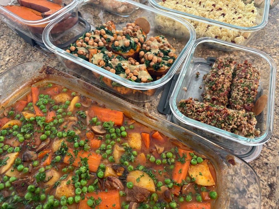 A collection of glass meal prep containers featuring beef burgundy, pecan-crusted halibut fillets, and roasted sweet potatoes topped with chickpeas and spinach in sauce.