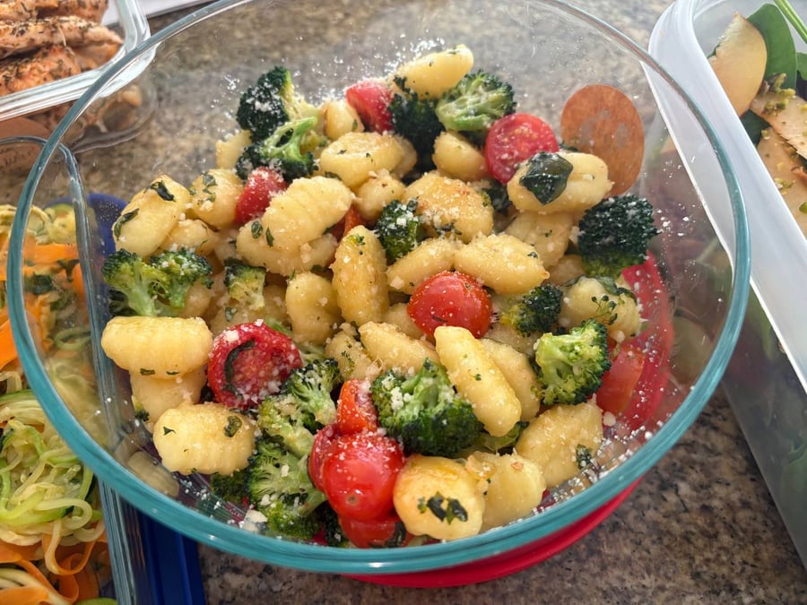 A glass bowl filled with potato gnocchi tossed with roasted broccoli florets, vibrant cherry tomatoes, and a light dusting of finely grated parmesan cheese.