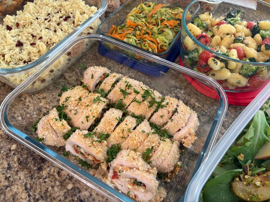 A glass container featuring sliced tomato, basil, and feta stuffed chicken roll ups garnished with fresh parsley and arranged in a meal prep dish.