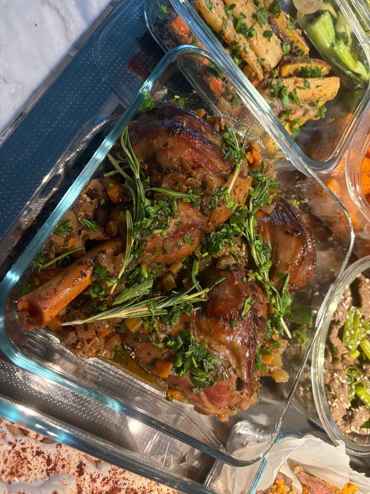 Braised lamb shanks with herbs and vegetables in a glass container.
