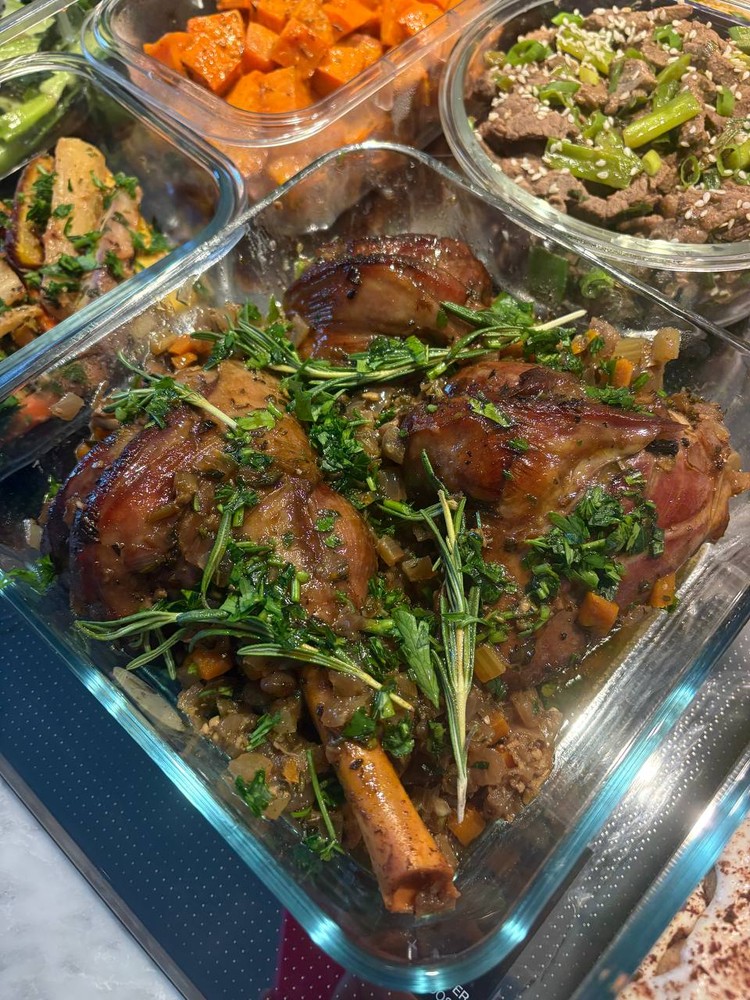 Close-up of braised lamb shanks garnished with fresh herbs.