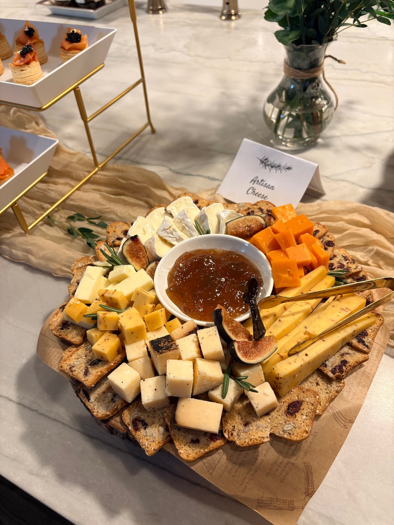 Sliced and cubed cheeses, crackers and a bowl of preserves on a round wooden board.