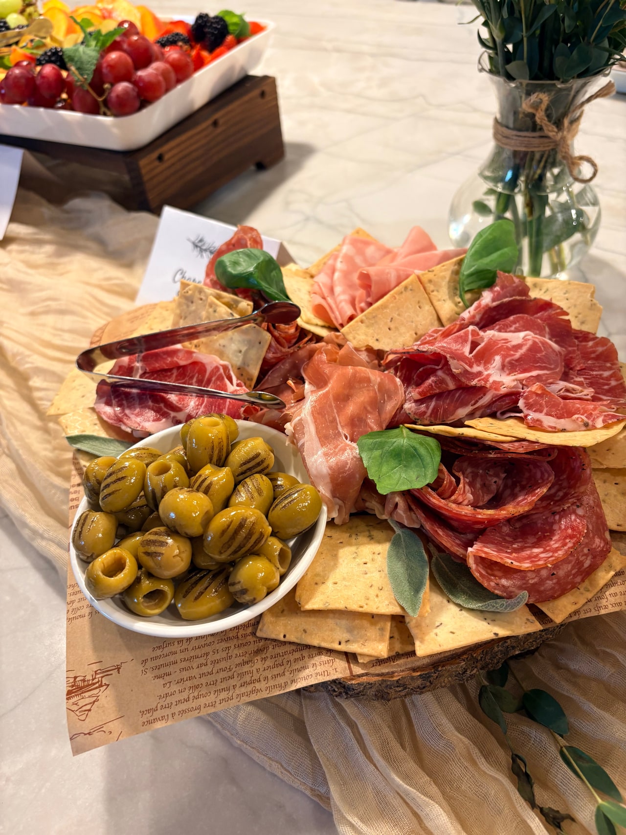 A charcuterie board with cured meats, olives, crackers and a small basil garnish.