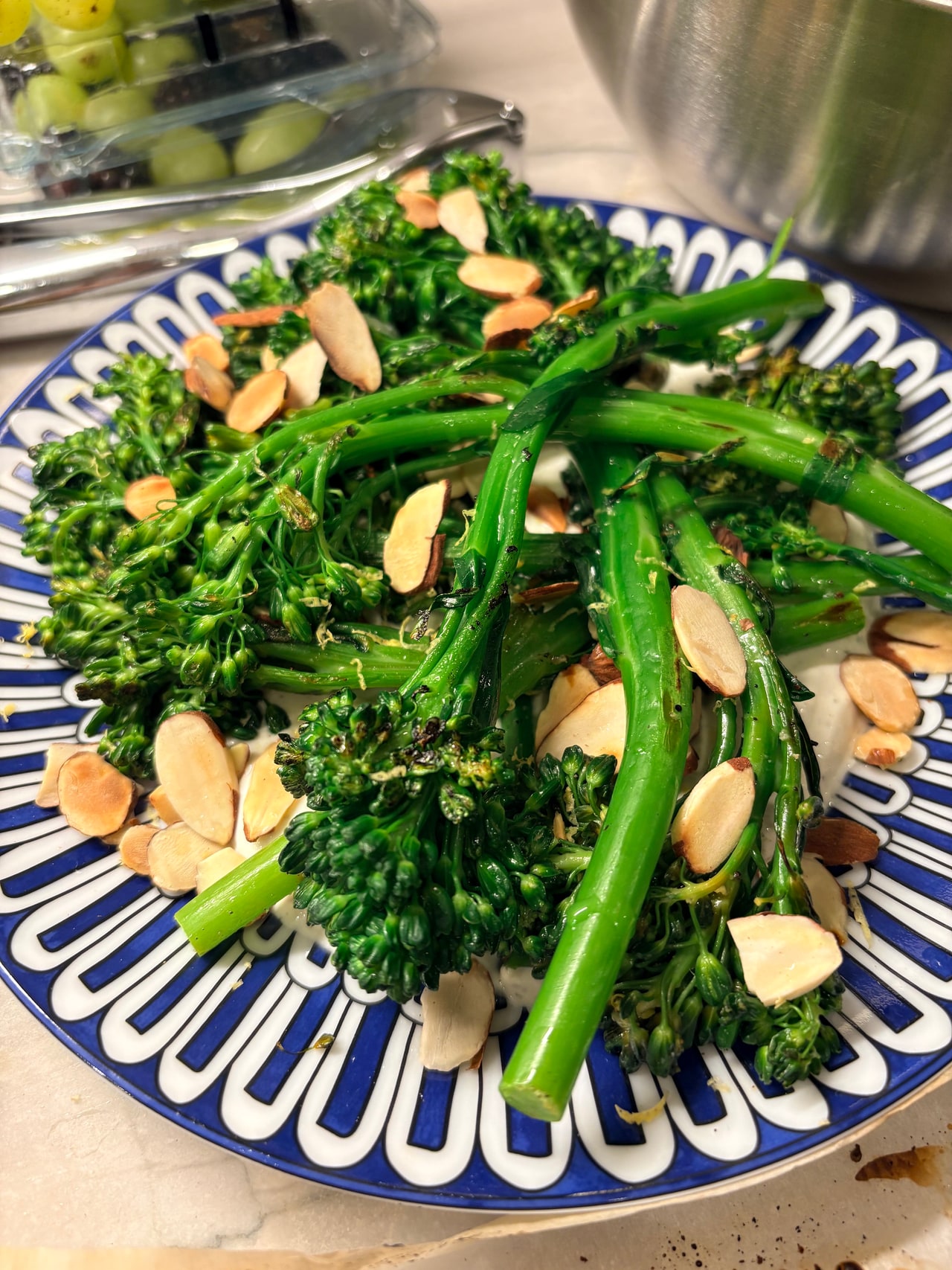 Charred broccolini topped with sliced almonds on a blue-and-white platter.
