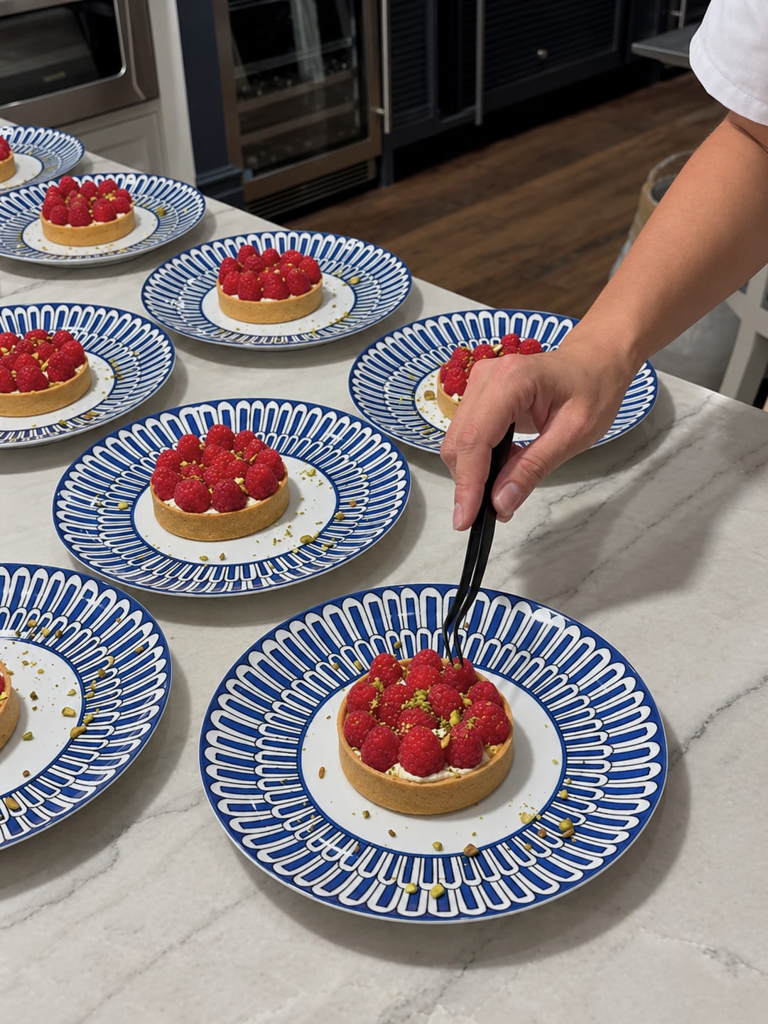 A chef finishes raspberry tartlets on blue-and-white dessert plates at the kitchen counter.