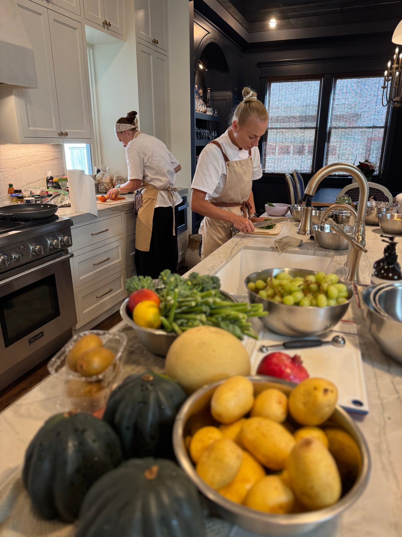 Two chefs prepare ingredients beside a fruit-covered counter in a home kitchen.