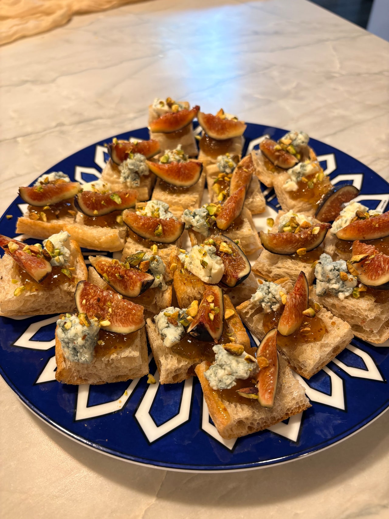 Fig and Gorgonzola crostini with preserves and chopped nuts arranged on a blue-and-white platter.