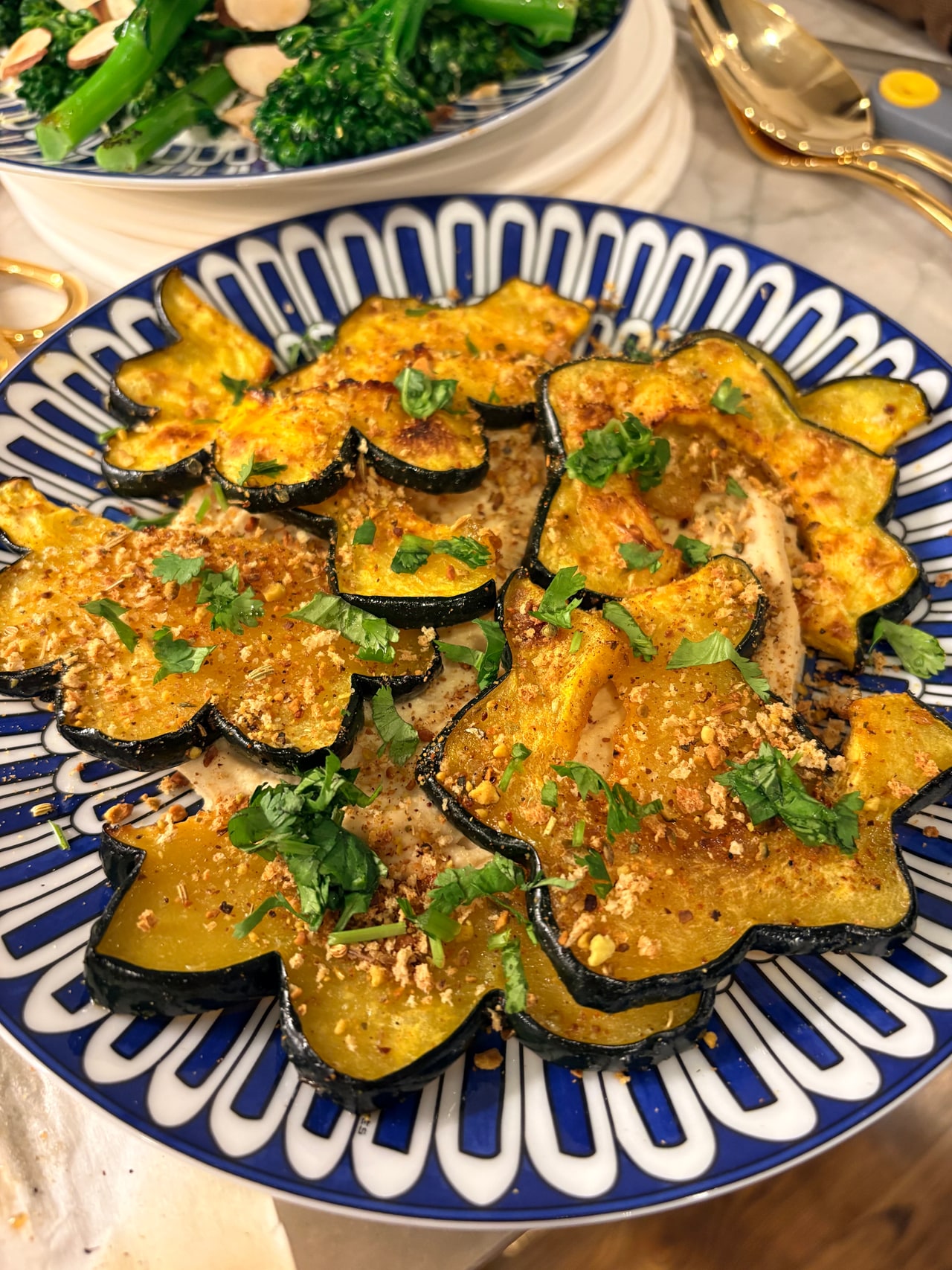 Slices of roasted acorn squash finished with a crumb topping and fresh herbs on a blue-and-white platter.