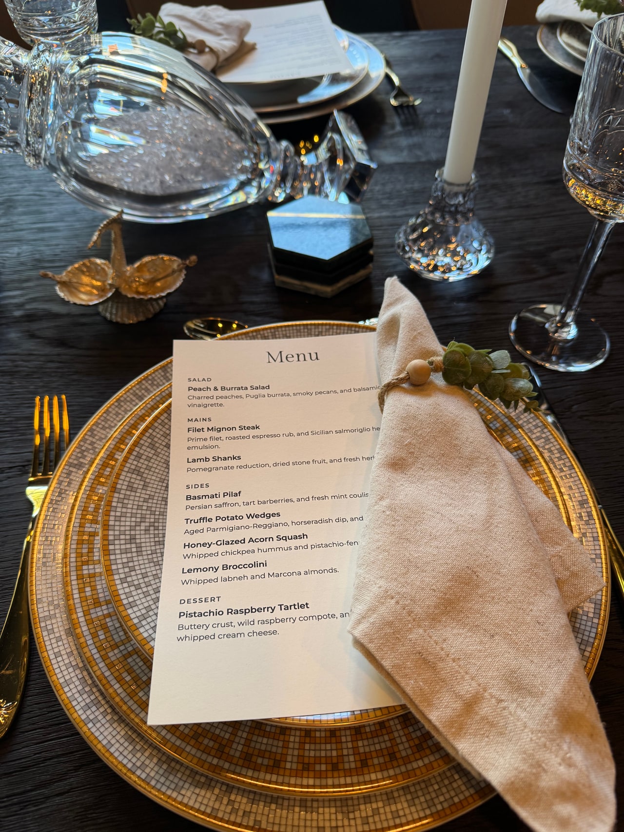 A closer view of the housewarming menu, napkin ring, gold cutlery and gold-rimmed plate.