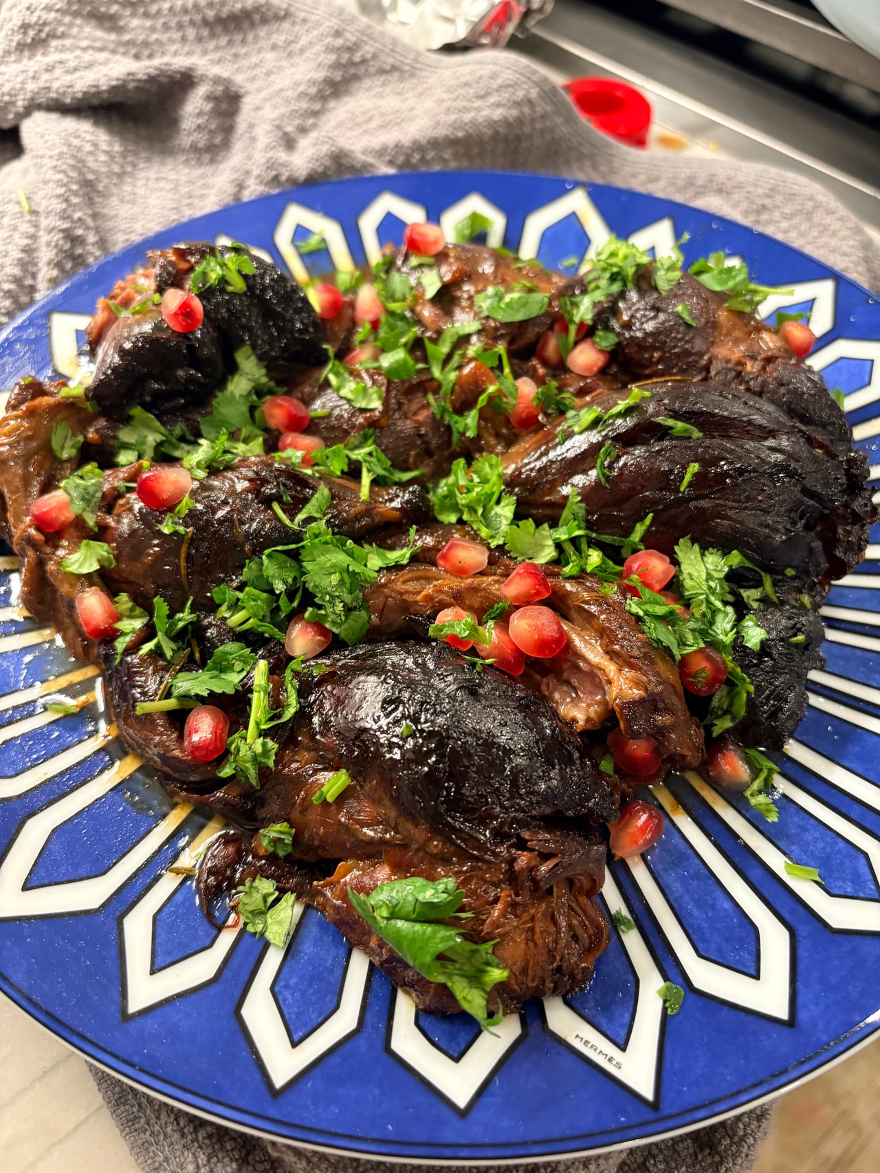 Braised lamb shanks topped with pomegranate seeds and fresh herbs on a blue-and-white serving platter.