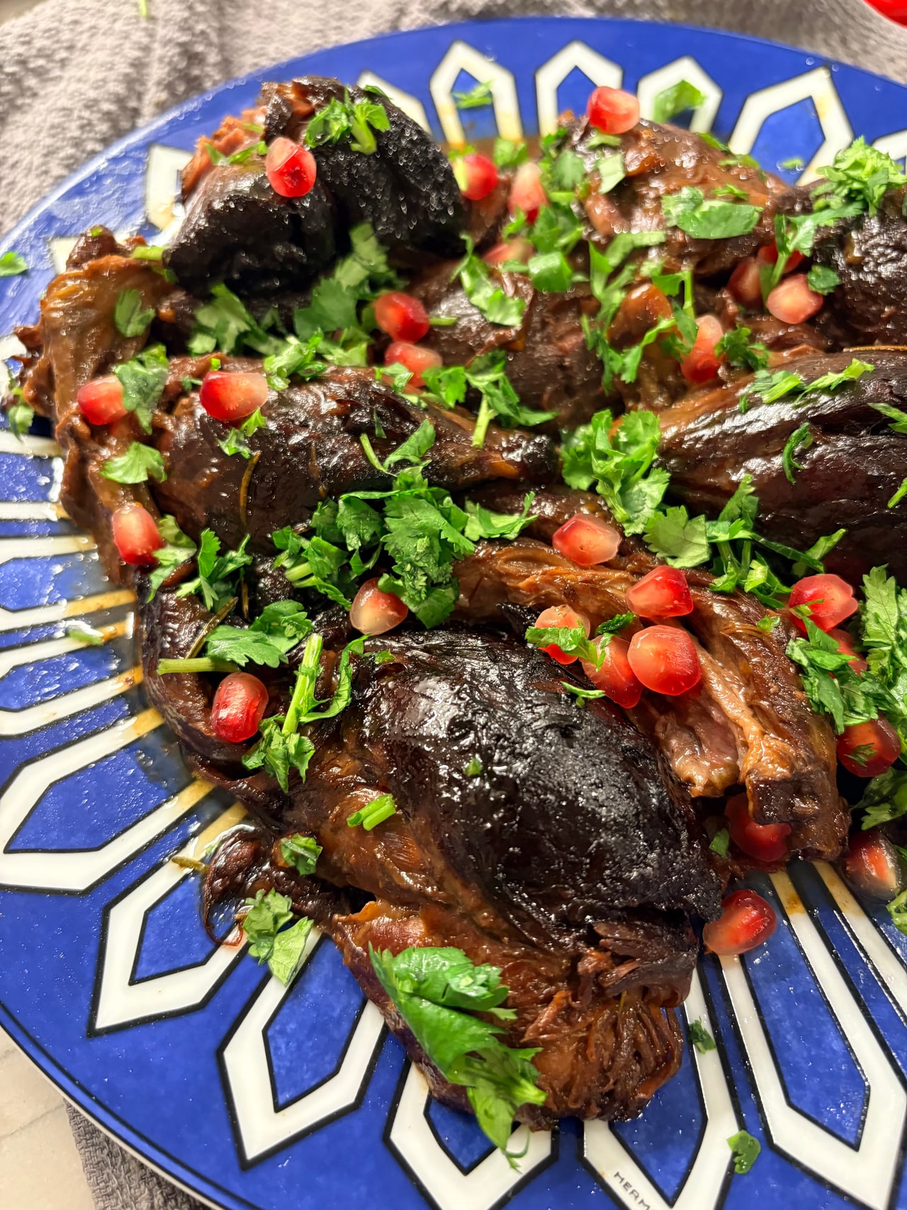 A close view of braised lamb shanks, glossy sauce, pomegranate seeds and fresh herbs.