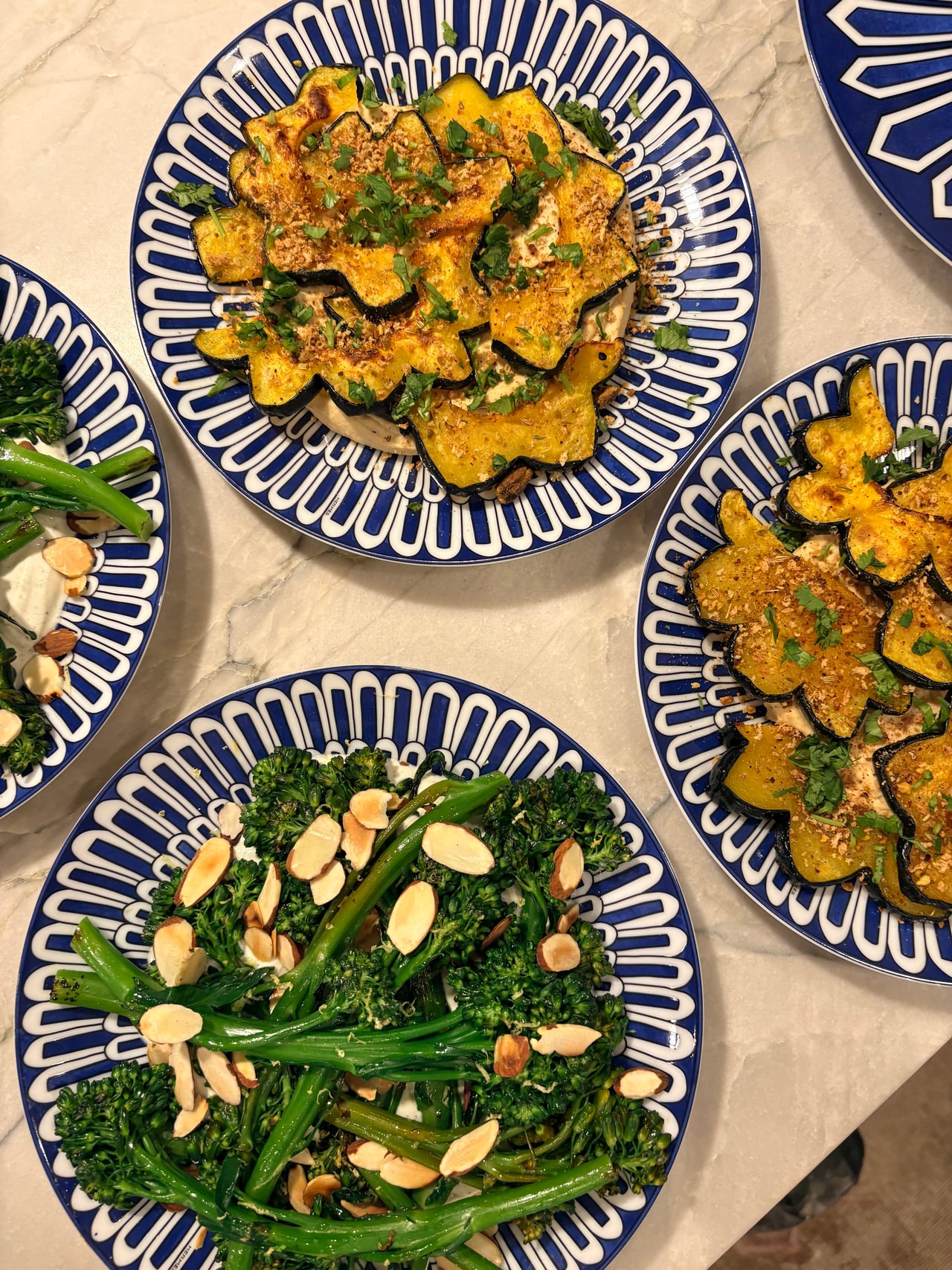 Blue-and-white platters of roasted acorn squash and broccolini with sliced almonds.