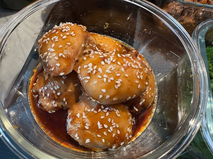 Close-up of sesame chicken drumsticks in a glass container.