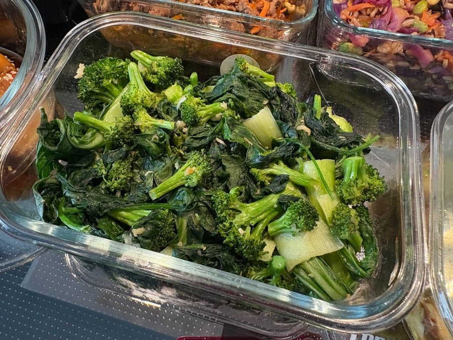 Close-up of sautéed broccoli and greens in a glass container.